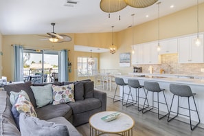 A modern living room with a sofa, a coffee table, and a kitchen area with a bar and high chairs.