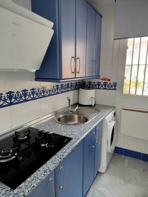 A kitchen with blue cabinets, a stainless steel sink, a washing machine, and a stove. - Apartment near a magical spot in Chiclana (Poblado de Sancti Petri)