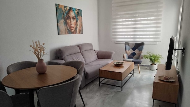 Ett modernt vardagsrum med en soffa, ett soffbord, ett matbord med stolar, en tv och ett fönster med persienner.