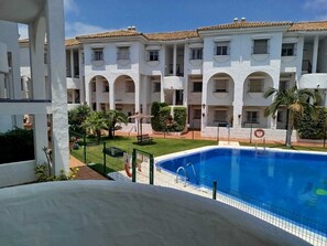 A poolside view of a building with multiple balconies and a swimming pool. - Apartment near a magical spot in Chiclana (Poblado de Sancti Petri)