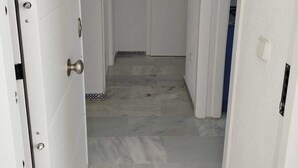 En smal hall med vita väggar och ett klinkergolv, som leder fram till en dörr med en handdukshängare ovanför.