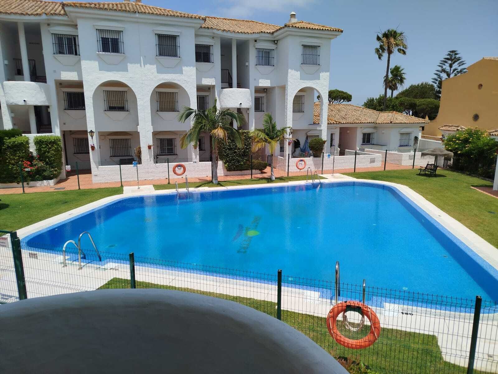 A swimming pool with a fence, a lifebuoy, and a building with multiple balconies.