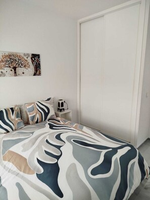 A bedroom with a bed, pillows, a nightstand, a wall art piece, and a wardrobe. - Apartment near a magical spot in Chiclana (Poblado de Sancti Petri)