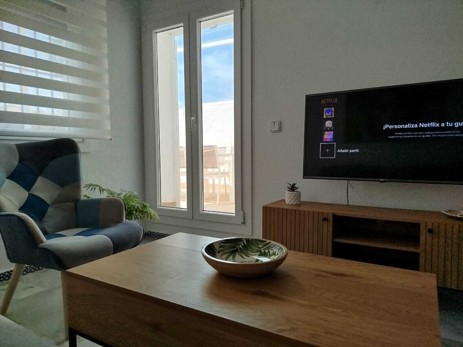 A living room with a large flat-screen TV mounted on the wall, a sofa, a coffee table with a bowl, and a sliding glass door leading to an outdoor area.