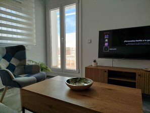 A living room with a large flat-screen TV mounted on the wall, a sofa, a coffee table with a bowl, and a sliding glass door leading to an outdoor area. - Apartment near a magical spot in Chiclana (Poblado de Sancti Petri)