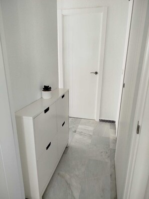 A narrow hallway with a white door, a small cabinet with drawers, and a tiled floor. - Apartment near a magical spot in Chiclana (Poblado de Sancti Petri)