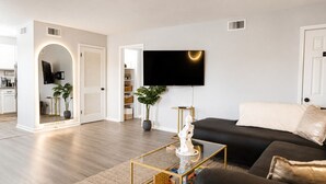 Ein modernes Wohnzimmer mit Flachbildfernseher, einer schwarzen Couch, einem Couchtisch und einem Topf mit Pflanze.