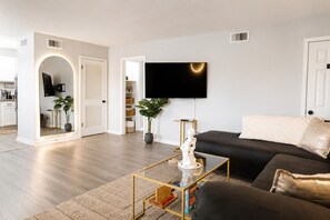 Ett modernt vardagsrum med en platt-TV, en svart soffa, ett soffbord och en krukväxt.