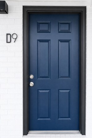 A dark blue door with a rectangular panel design, a numeric address sign '09' to the left, and a metal door handle. - 2BR Atlanta Home Base: Airport Access + Workspace (Jonesboro)