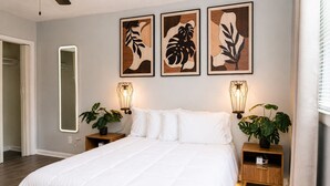 Ein Schlafzimmer mit einem großen Bett, Nachttischen mit Pflanzen, Wandlampen und gerahmten Bildern.