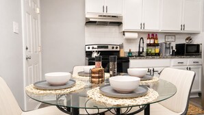Eine moderne Küche mit weißen Schränken, einem Glastisch mit Platzsets und einer Kaffeestation.