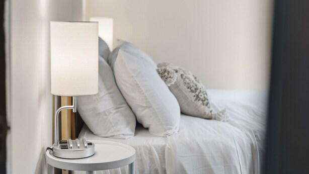 Ein ordentlich bezogenes Bett mit weißer Bettwäsche und ein Nachttisch mit einer Lampe.