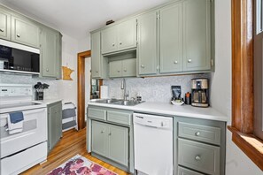 A kitchen with light green cabinets, a white stove, a dishwasher, and a coffee maker. - Magnolia House (Minneapolis)
