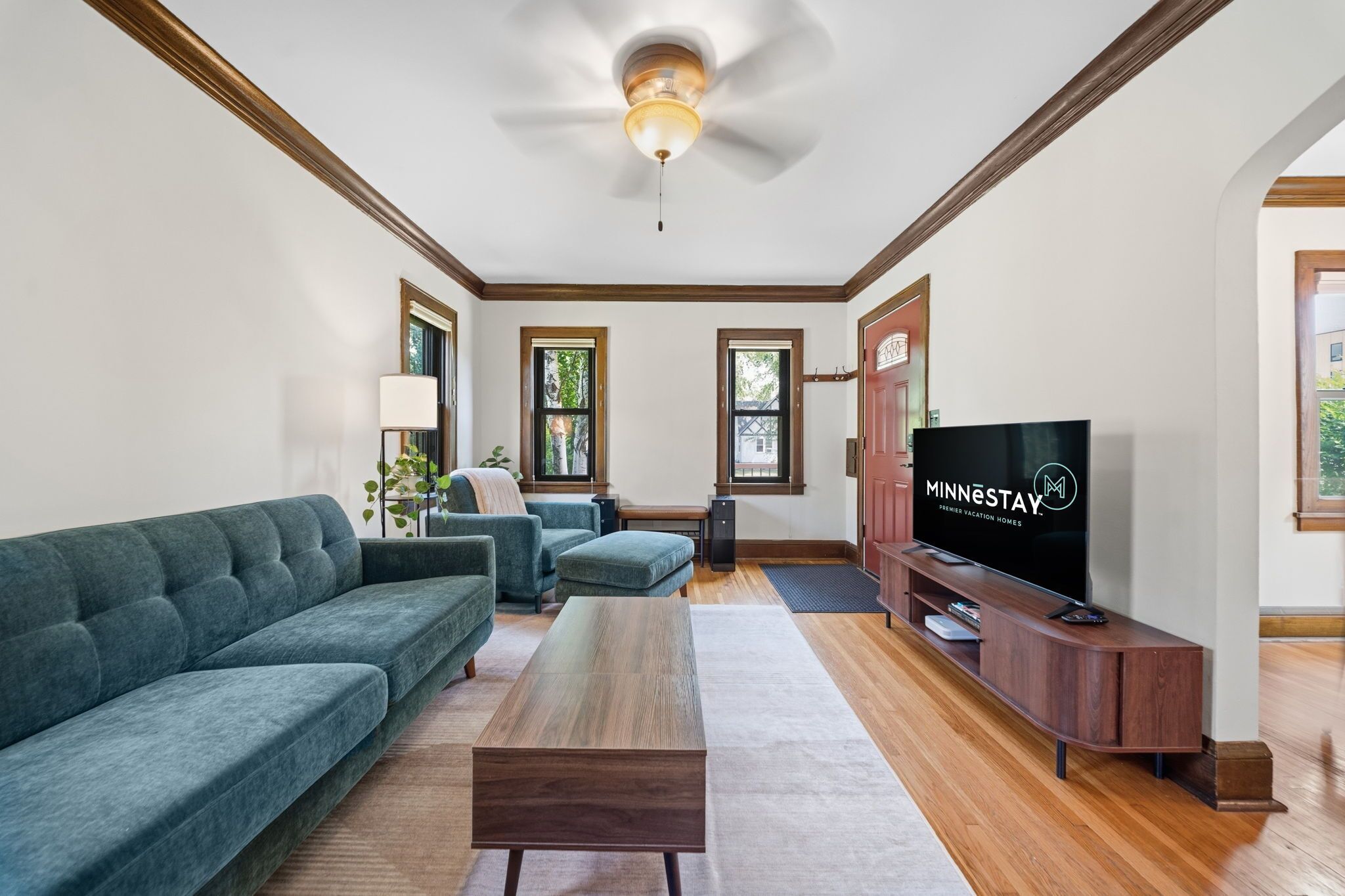 A modern living room with a sectional sofa, a coffee table, a TV on a wooden stand, and a ceiling fan.