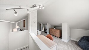 Ein modernes Schlafzimmer im Loft-Stil mit schrägwand, weißem Heizkörper, einem Holztisch, einem dunklen Sitzsack und einer kleinen Holzkommode.