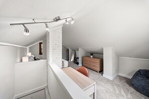 Ein modernes Schlafzimmer im Loft-Stil mit schrägwand, weißem Heizkörper, einem Holztisch, einem dunklen Sitzsack und einer kleinen Holzkommode.