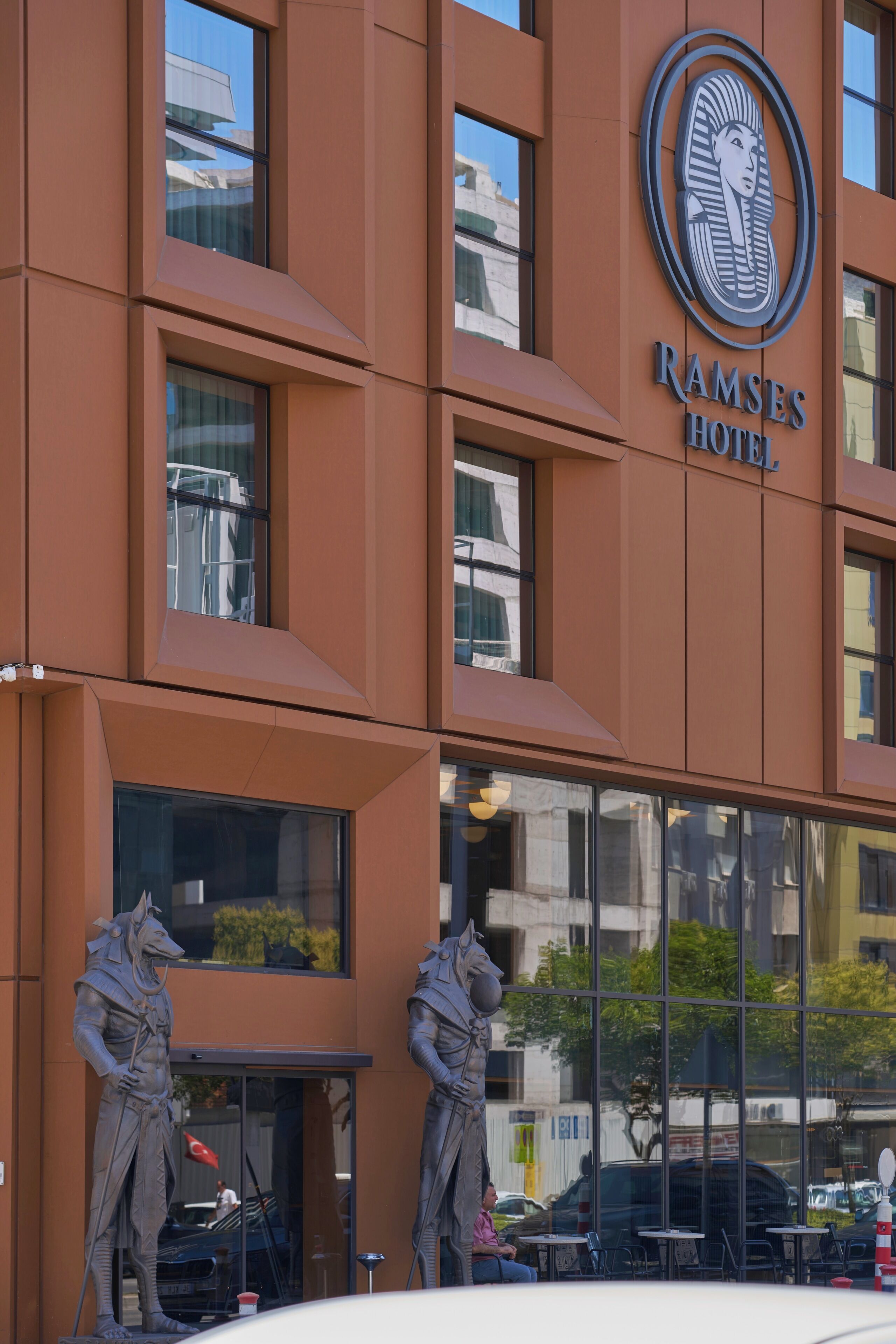 A modern building with a prominent hotel sign, large windows, and two statues at the entrance.