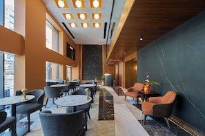 A modern hotel lobby with round tables, comfortable seating, a marble floor, and a large black wall with a marble pattern. - RAMSES HOTEL (Izmir)
