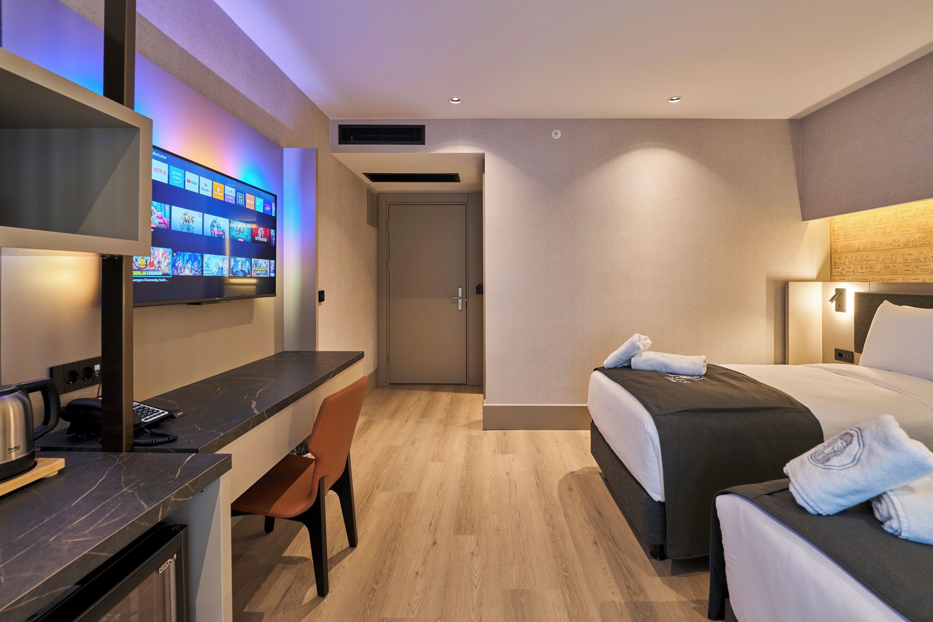 Habitación de hotel con escritorio, silla, cama y televisor que muestra un servicio de streaming.