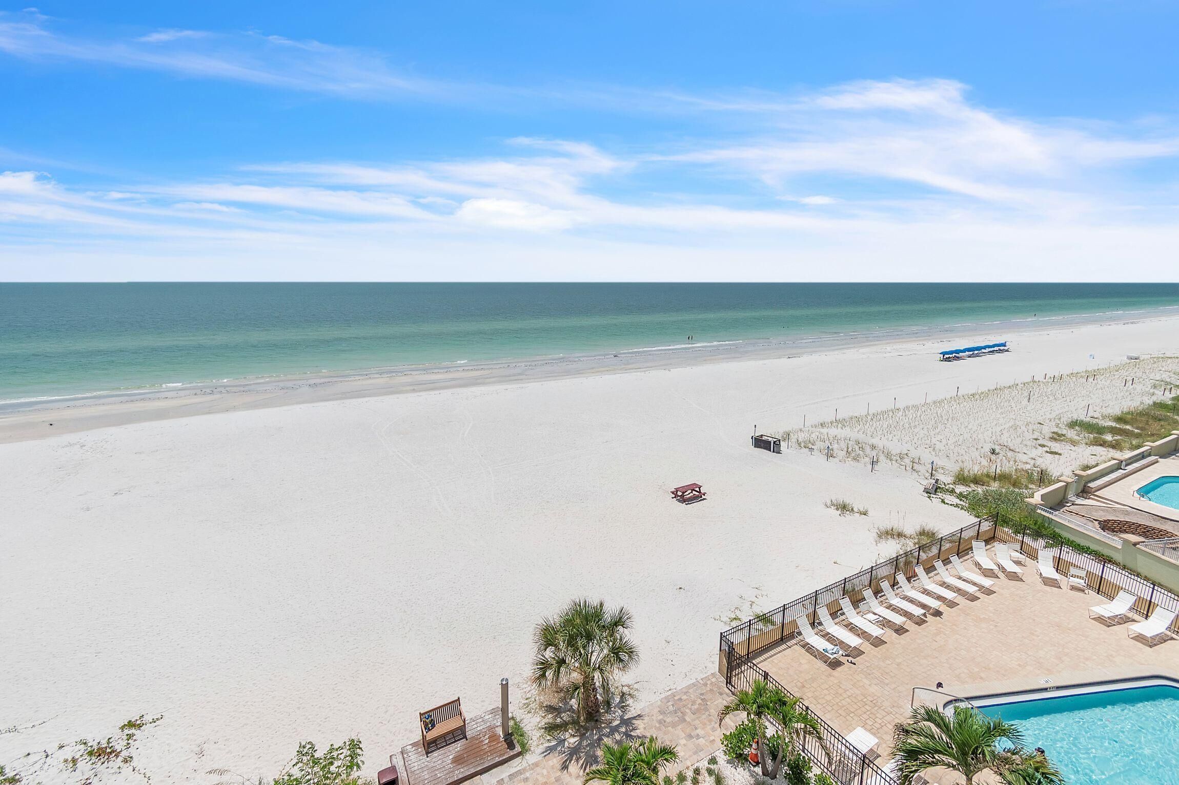 A beach view with a pool area, lounge chairs, and a lifeguard stand.