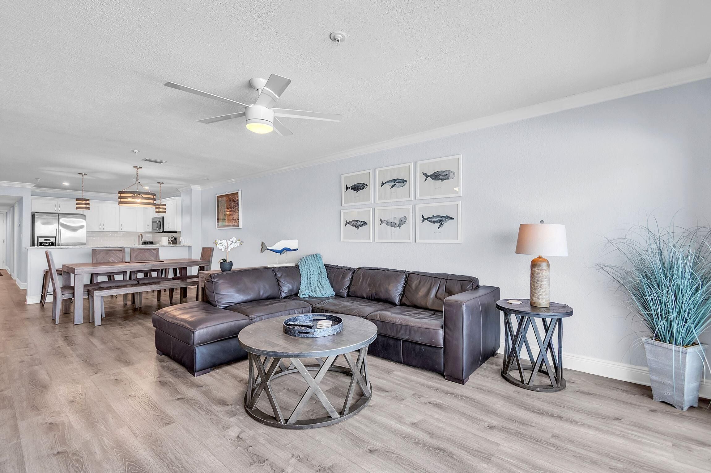A modern living room with a sectional sofa, a round coffee table, a dining area with a bench, and a kitchen in the background.
