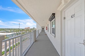 A long, narrow balcony with a railing, white doors, and a clear view of the street and buildings in the distance. - Seagate 407 (Indian Shores)