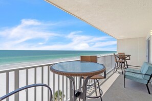 A balcony with a glass table, wicker chairs, and a view of the beach and ocean. - Seagate 407 (Indian Shores)