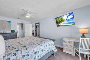 A bedroom with a bed, a desk, a chair, a ceiling fan, and a wall-mounted TV. - Seagate 407 (Indian Shores)
