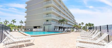 Un hotel con piscina, varios balcones y sillones de sol.
