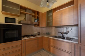 A modern kitchen with wooden cabinets, a stainless steel sink, and a built-in microwave. - Villa Micelli by BarbarHouse (Campomarino)