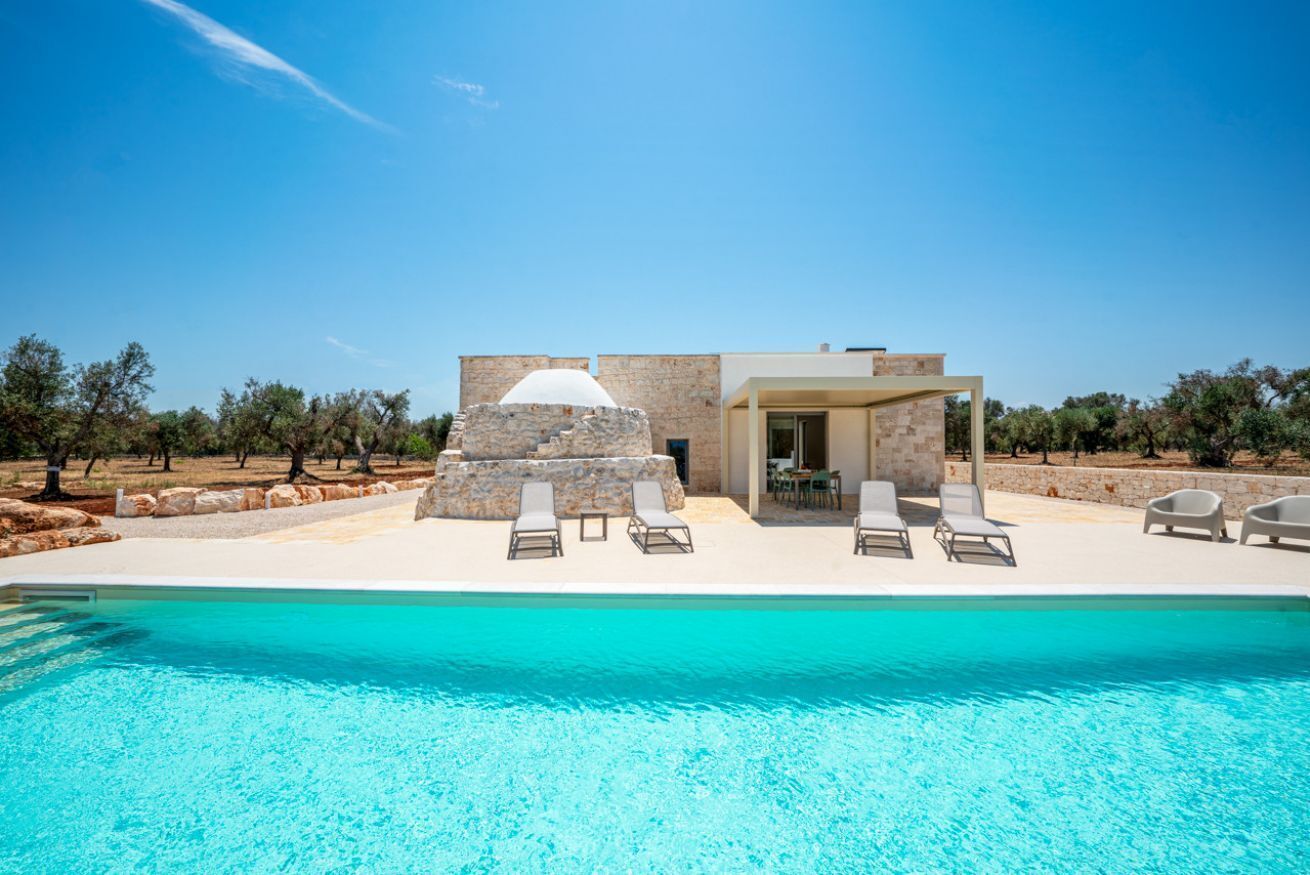 A pool with clear water, a stone structure, and lounge chairs.