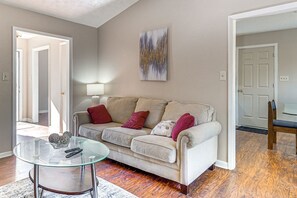 A living room with a beige sofa, a glass coffee table, and a painting on the wall.
