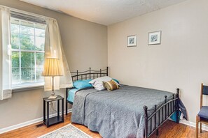 A bedroom with a bed, a nightstand, a lamp, a chair, and a window with curtains.