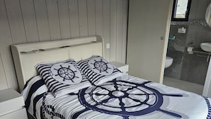 Un lit avec une couvre-lit à motifs nautiques, une tête de lit en bois et une vue sur la salle de bain.