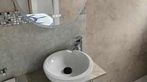 Une salle de bain avec un miroir rond, un lavabo blanc et une baignoire.
