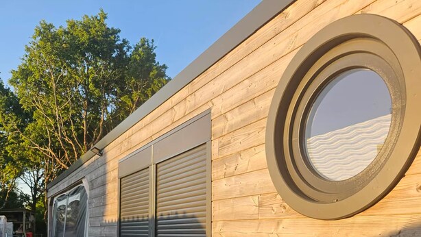 Un mur extérieur en bois, doté d’une fenêtre circulaire et d’une porte coulissante.