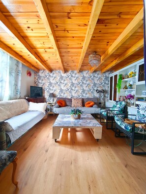 A wooden ceiling with exposed beams, a patterned wall, a sofa with cushions, a coffee table with a plant, and a chair with a cushion.