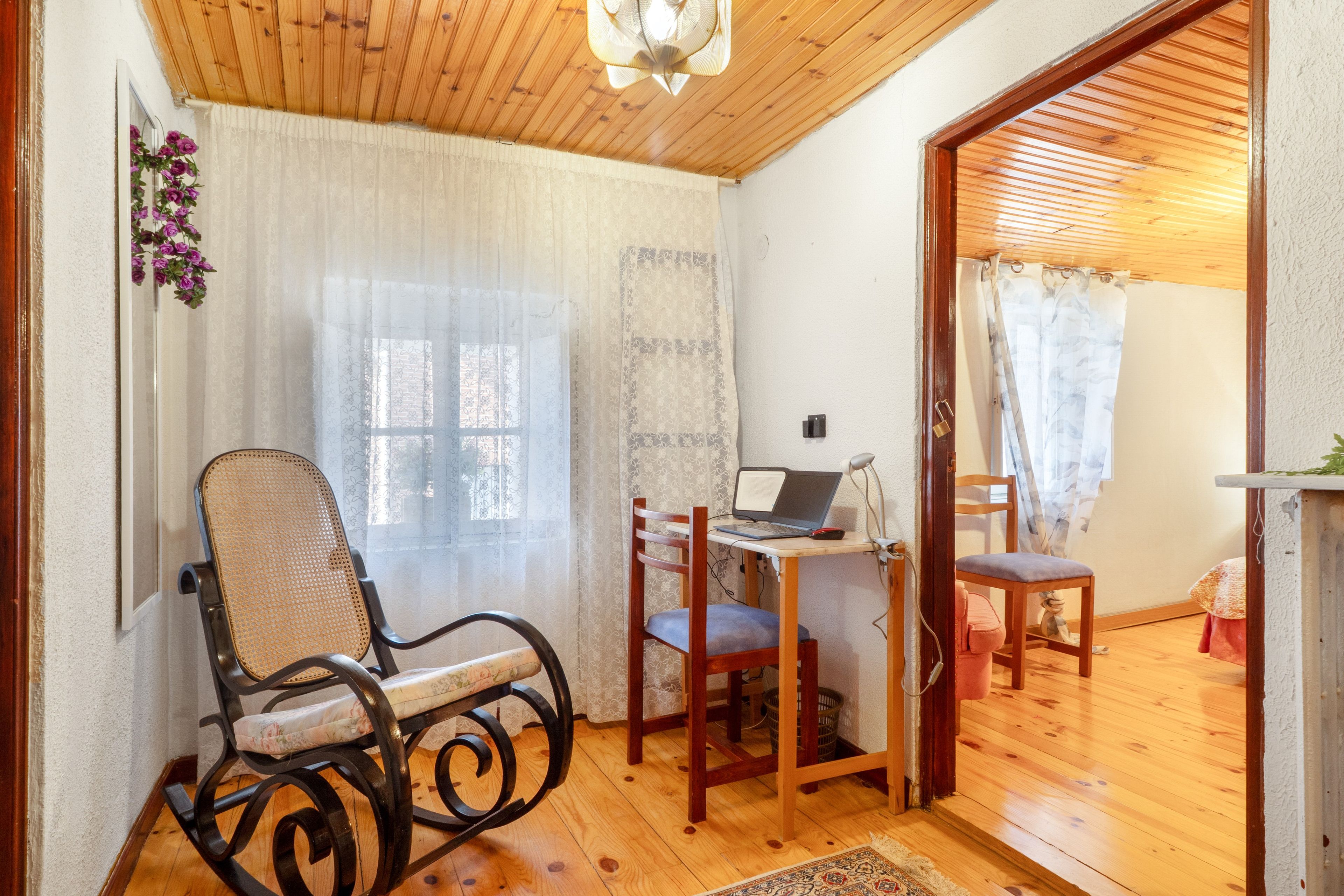 A room with a wooden ceiling, a desk with a laptop, a chair, and a window with curtains.