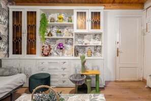 Une pièce avec un meuble blanc aux portes vitrées, un arbre à chat vert et un canapé gris.
