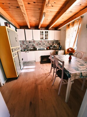 A kitchen with wooden beams, white cabinets, a tiled backsplash, and a dining area with a table and chairs.