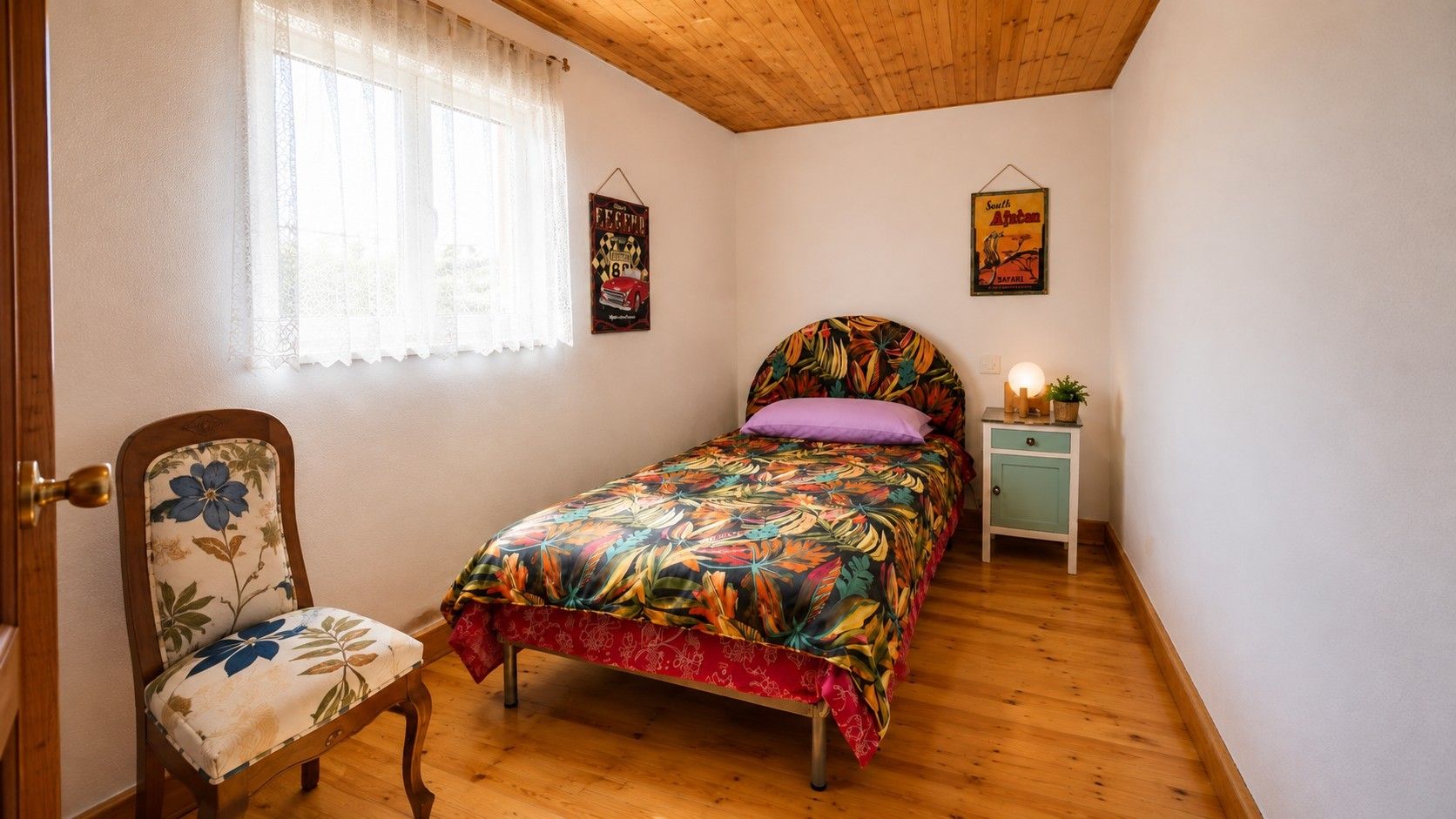 Un dormitorio con cama, una silla, una mesita de noche y una ventana con cortinas.