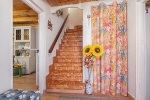 A wooden staircase leading to a room with a floral curtain and a vase with sunflowers.