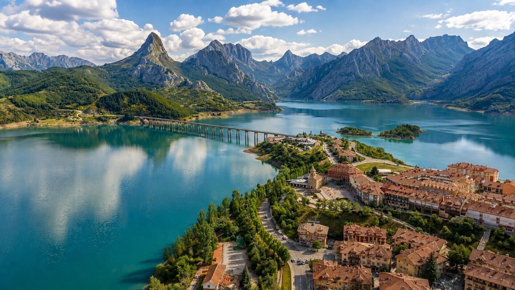 Un pueblo costero con un puente, un lago y montañas al fondo.