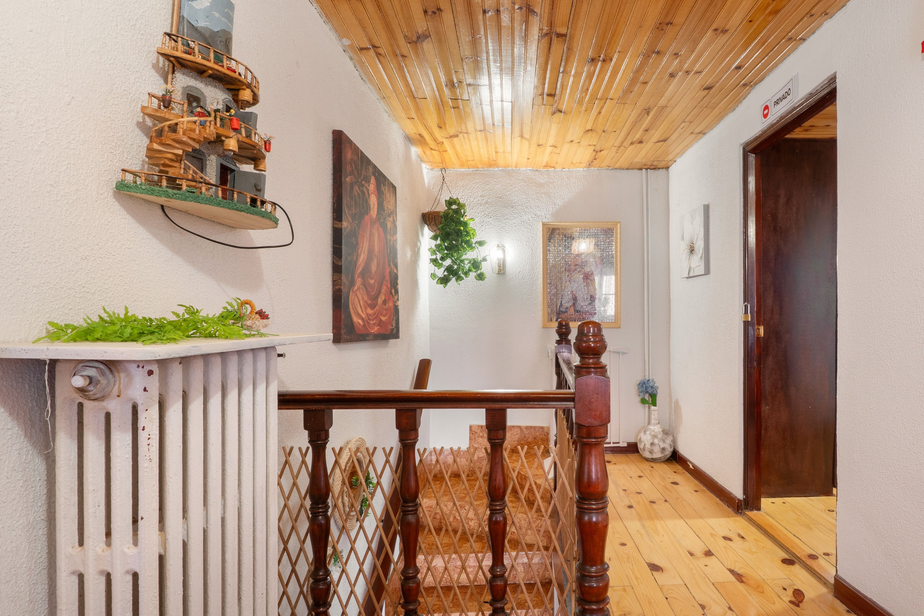 Una escalera de madera que lleva a una puerta, un radiador y una pequeña mesa con plantas.