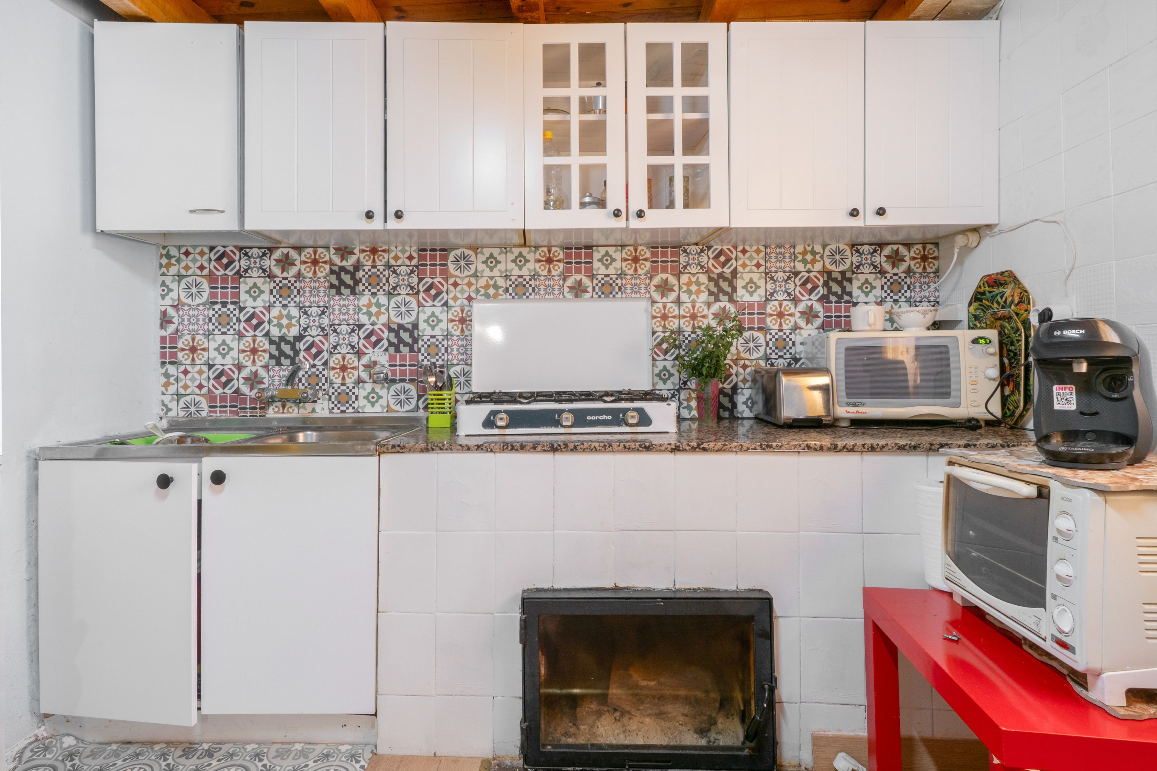 Una cocina compacta con armarios blancos, un salpicadero estampado y una encimera roja.