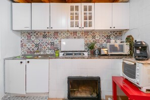 Une cuisine de taille réduite avec des meubles blancs, un pare-feu décoré et un plan de travail rouge.