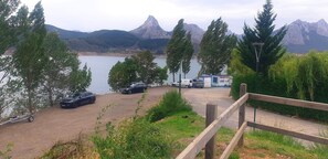 Un espace de stationnement avec des véhicules, une clôture en bois et une vue sur un lac, avec des montagnes en arrière-plan.