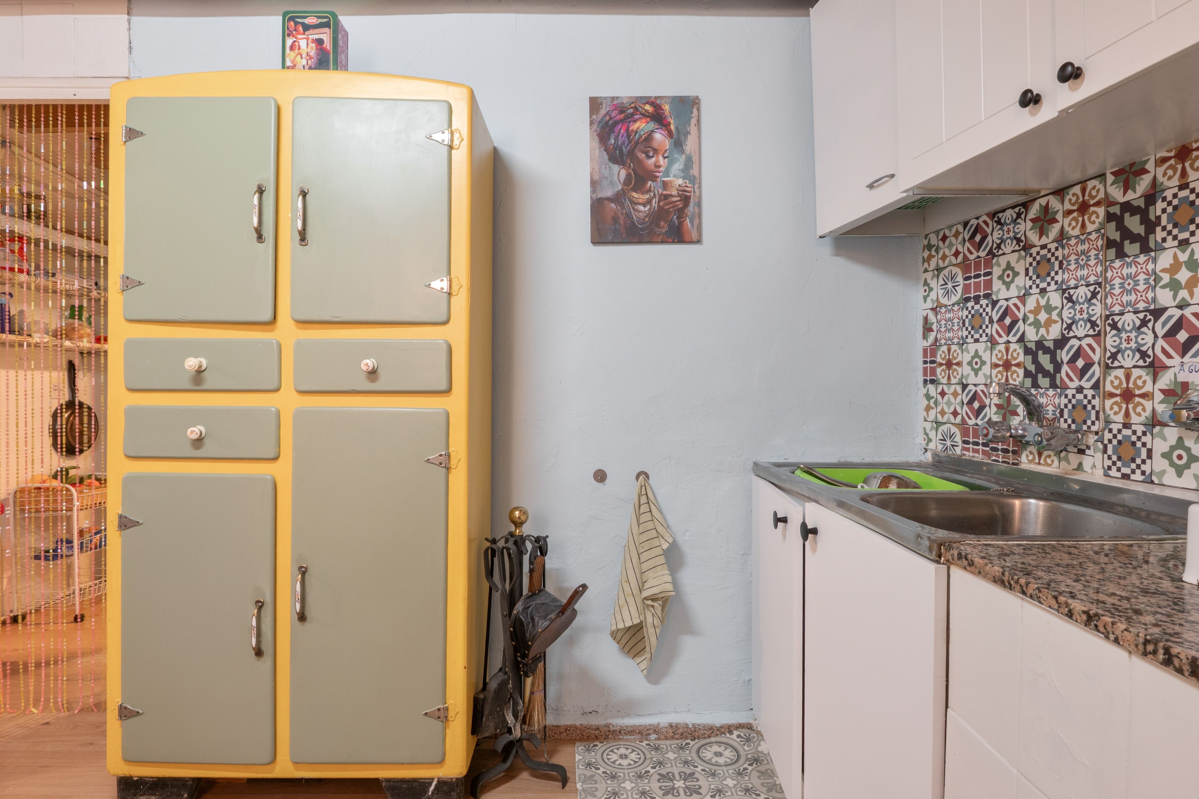Een keuken met een vintage, gele koelkast, een betegelde spatwand met een patroon, en een enkel schilderij.