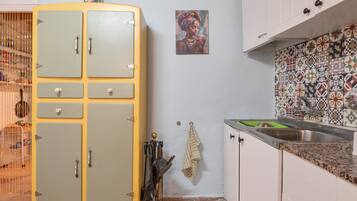 Een keuken met een vintage, gele koelkast, een betegelde spatwand met een patroon, en een enkel schilderij.