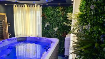A hot tub with a blue interior, surrounded by a wall of greenery and a white curtain.